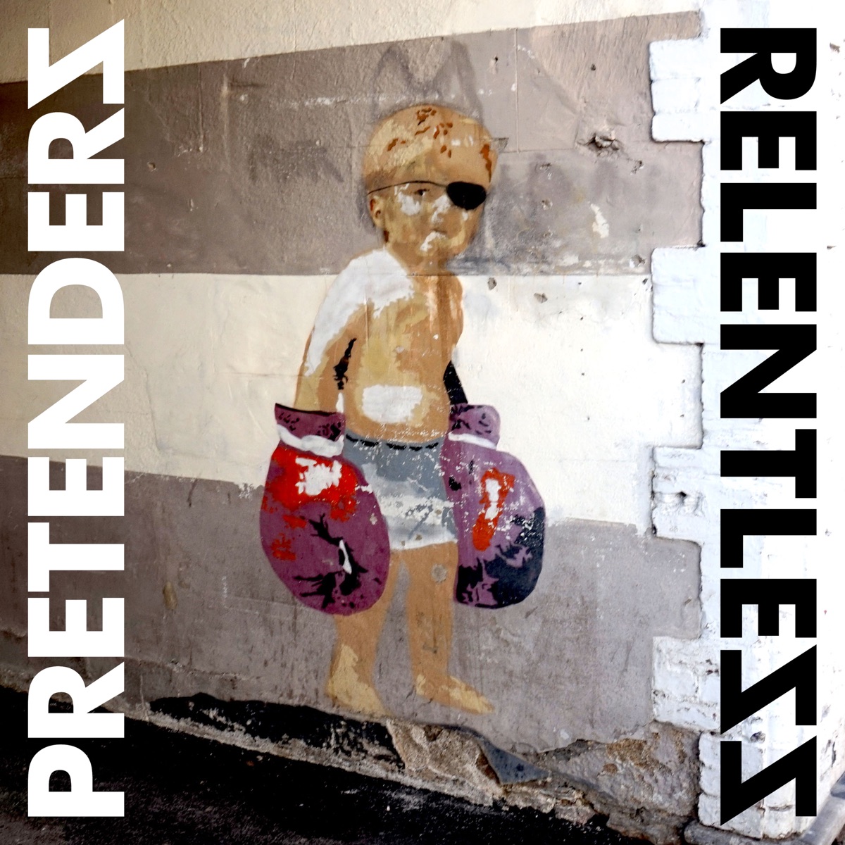 Streetart-ähnliches Cover mit einem Kind in Shorts, Augenklappe und übergroßen Boxhandschuhen vor grauer Wand. Albumcover von The Pretenders – Relentless.
