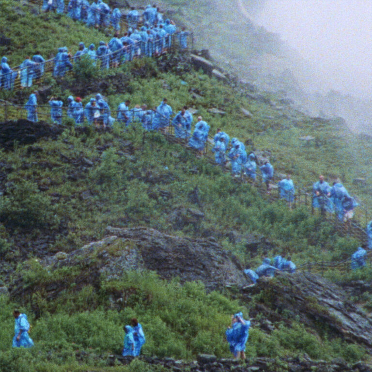 Albumcover von Courtney Barnett – End of the Day: Menschen in blauen Regenponchos steigen im Nebel eine grüne Berghangtreppe hinauf, cineastisch und entrückt.