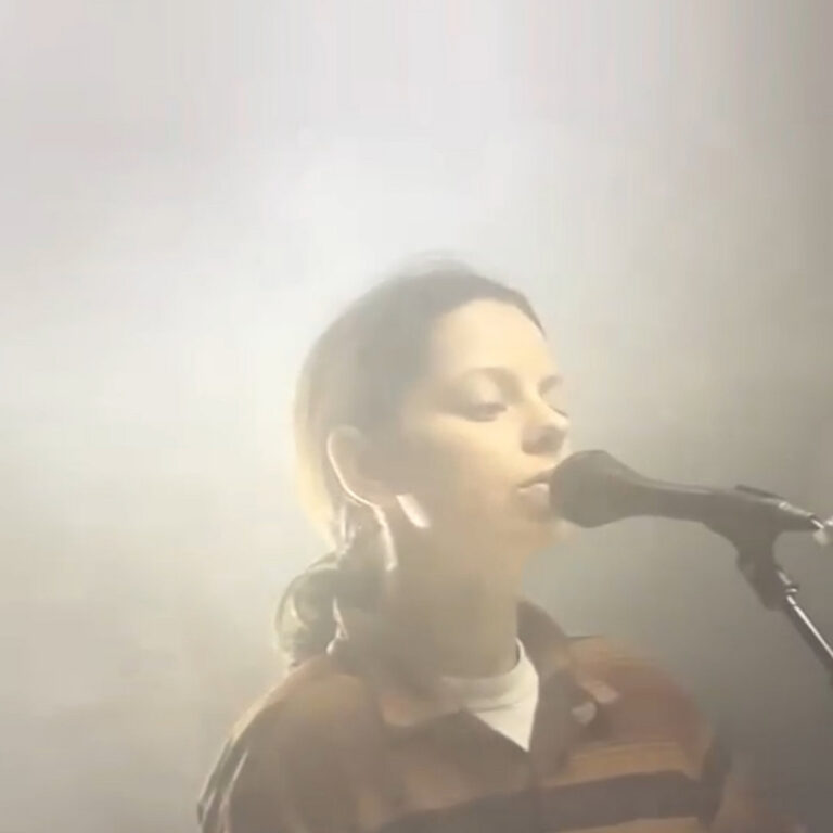 Vernebeltes Live-Foto von Tirzah beim Singen ins Mikrofon – minimalistisches, intimes Covermotiv zum Album „trip9love…???“.