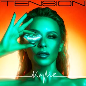 Kylie Minogue mit grünem Lichtfilter hält einen leuchtenden Diamanten vors Auge, vor orangenem Hintergrund – glamourös, futuristisch und sinnlich zugleich