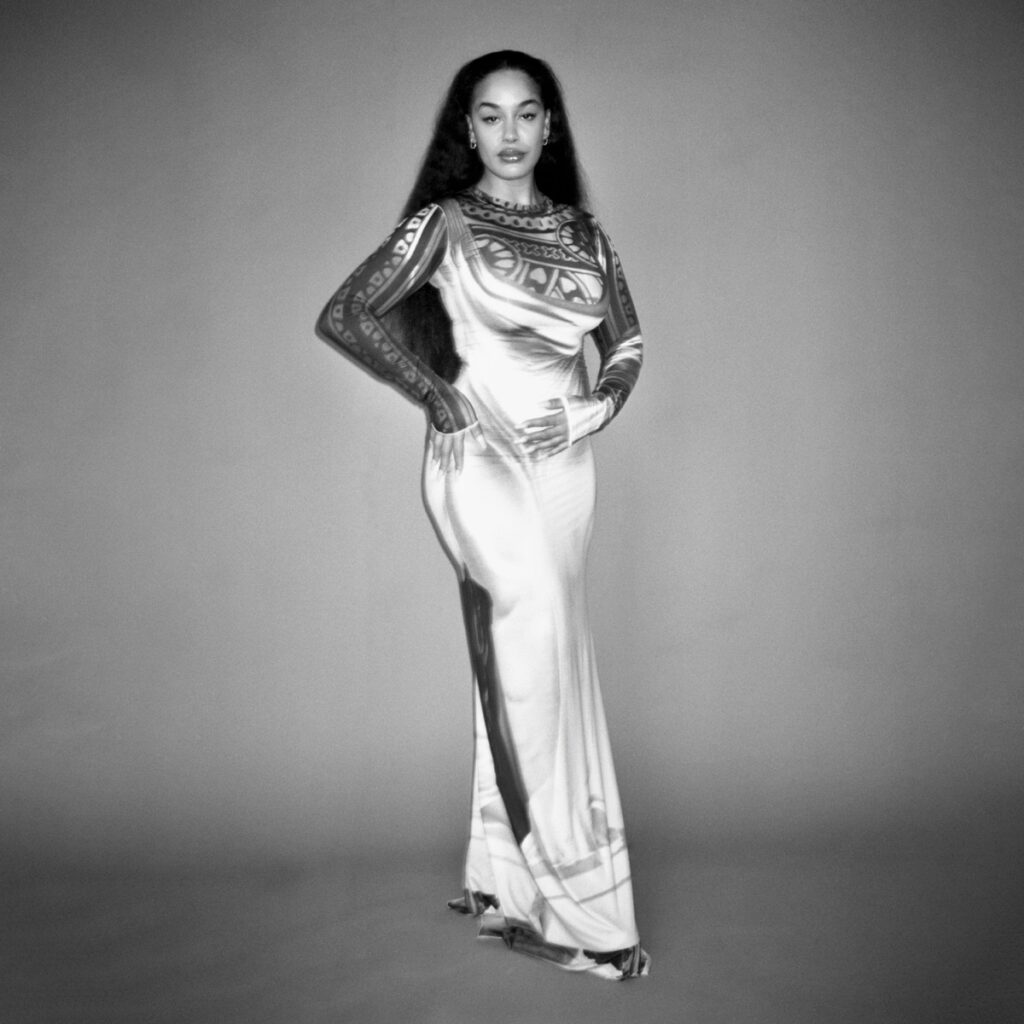 Albumcover zu „Falling or Flying“ von Jorja Smith – in einem langen, glänzenden Kleid steht sie selbstbewusst vor grauem Hintergrund, das Bild ist in Schwarz-Weiß gehalten.
