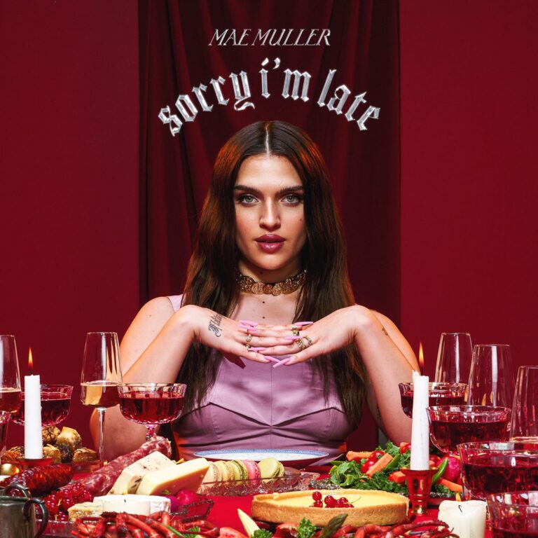 Albumcover zu „Sorry I’m Late“ von Mae Muller – sie sitzt inmitten eines reich gedeckten Tisches mit ernster Miene, violettem Kleid und königlicher Pose vor rotem Vorhang.