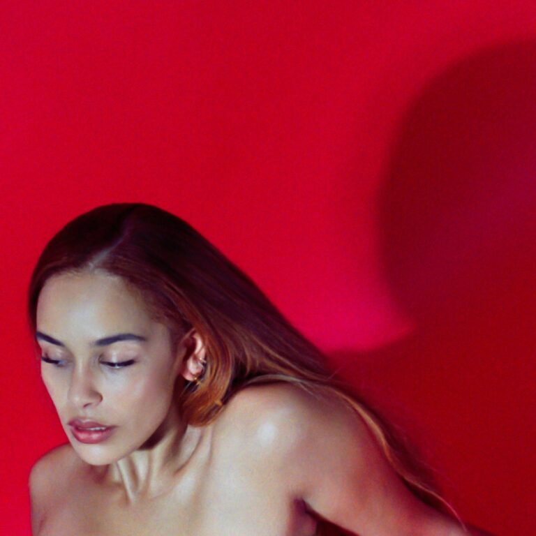 Porträtfoto von Jorja Smith vor knallrotem Hintergrund. Sie blickt mit geschlossenen Augen nach unten, die Schultern sind nackt, das Licht betont Haut und Haar. Der Schatten ihrer Silhouette fällt groß auf die Wand.