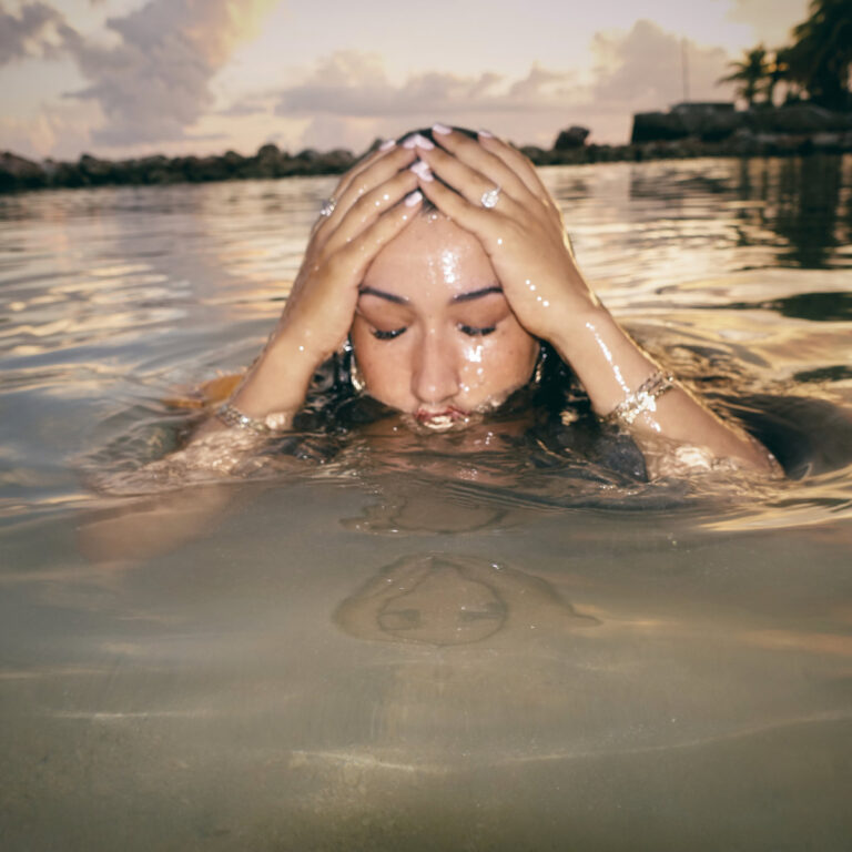 Cleo Sol mit geschlossenen Augen halb im Wasser versunken – ein Moment innerer Einkehr bei Sonnenuntergang.