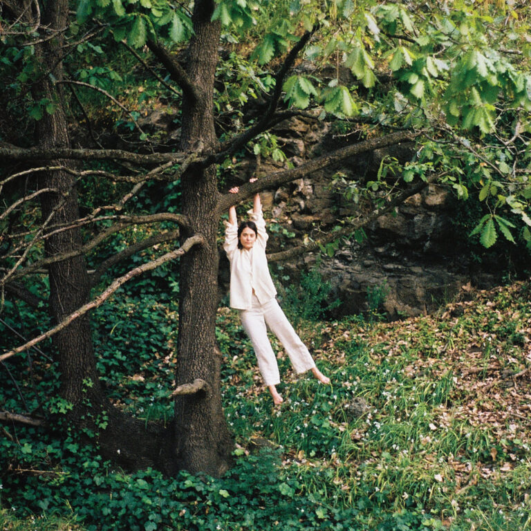 Das Albumcover von „To Enjoy is the Only Thing“ von Maple Glider zeigt Tori Zietsch barfuß in heller Kleidung, wie sie an einem Ast in einem grünen, bewaldeten Garten hängt – ruhig, naturverbunden und verletzlich.