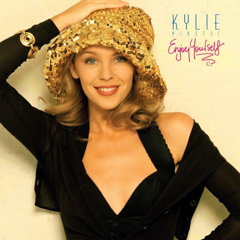 Kylie Minogue mit goldener Mütze lächelt in die Kamera, trägt ein schwarzes Oberteil.