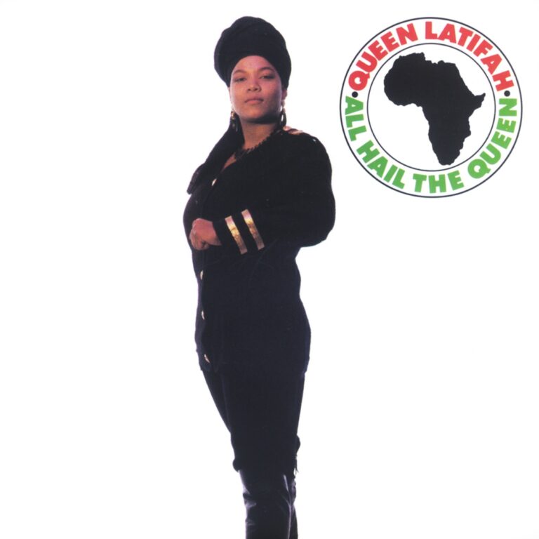 Queen Latifah posiert in einem schwarzen Outfit mit goldenen Akzenten vor einem weißen Hintergrund.