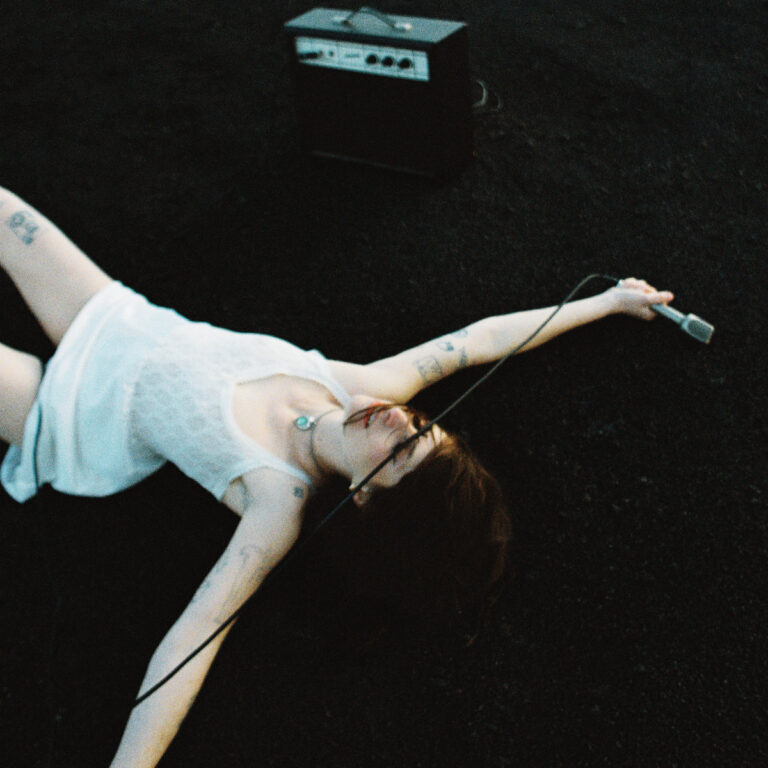 Cover des Albums „Sucker“ von IAN SWEET: Sängerin Jillian Medford liegt mit Mikro auf dunklem Boden, im Hintergrund ein kleiner Verstärker.