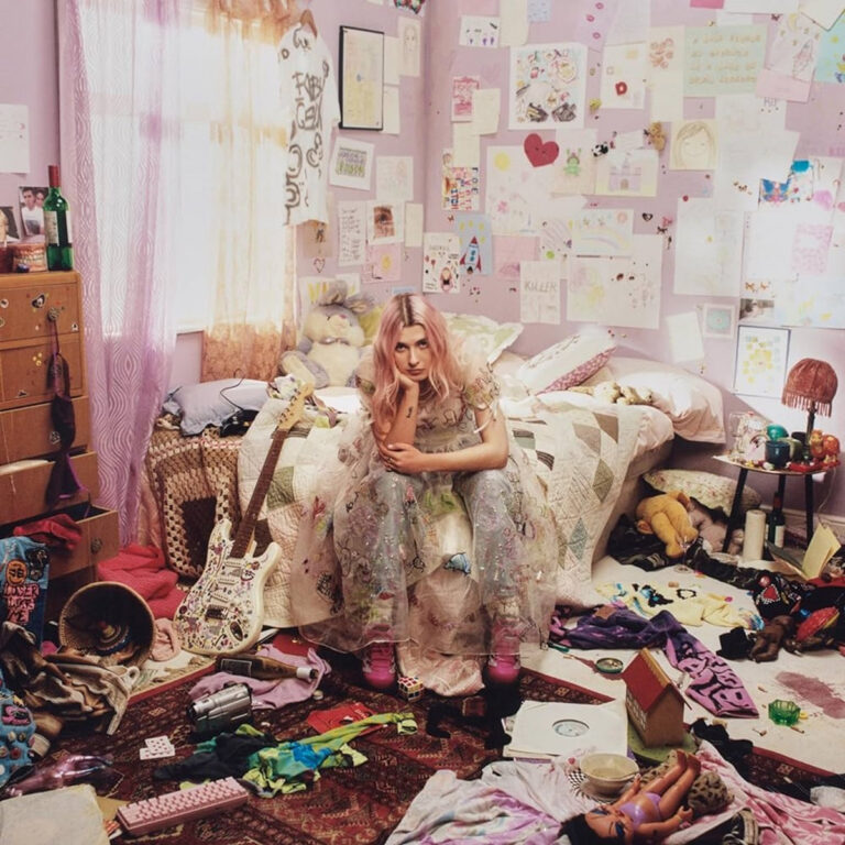 Albumcover von „Quarter Life Crisis“ mit Baby Queen im pinken, überfüllten Jugendzimmer – zwischen Spielzeug, Zeichnungen und Gitarren.