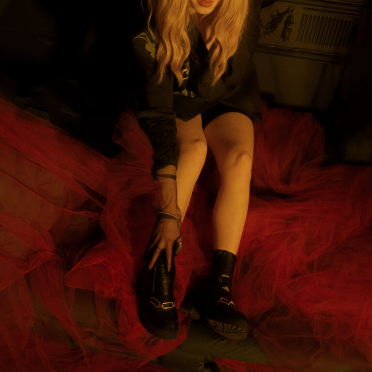 Cover der EP „Apple Juice“ von Niina – die Künstlerin sitzt auf rotem Tüll, im Halbdunkel, nur ihr blondes Haar, ihre Beine und schwarze Boots sind sichtbar.