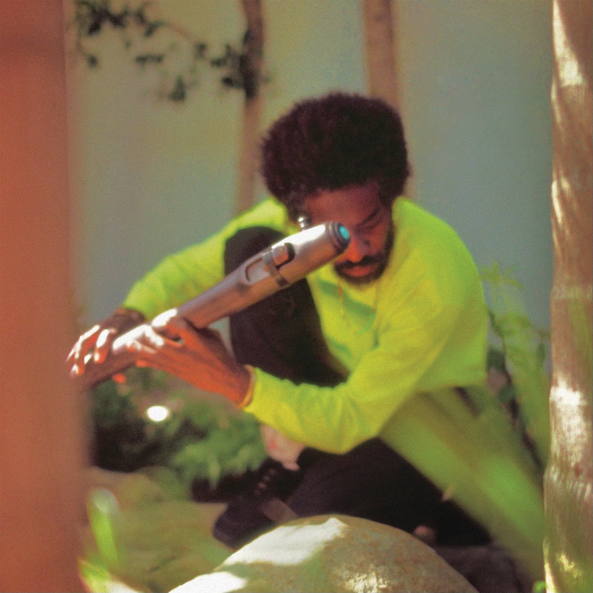 André 3000 sitzt mit Flöte im Freien, trägt ein neongelbes Shirt – stimmungsvolles, unscharf fotografiertes Coverbild seines Ambient-Albums „New Blue Sun“.