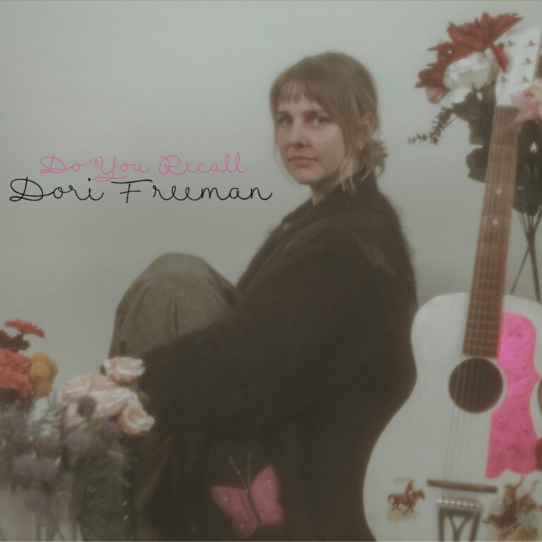 Dori Freeman sitzt zwischen Blumen neben einer verzierten weißen Gitarre – sanft verschwommenes Coverbild ihres Albums „Do You Recall“.