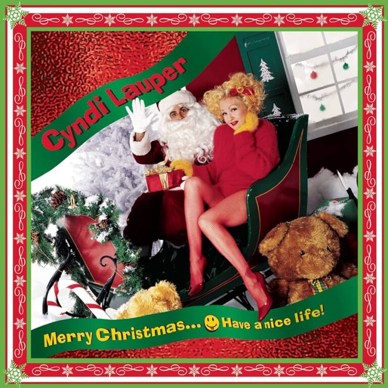 Cyndi Lauper sitzt in einem Schlitten neben einem Weihnachtsmann, umgeben von Geschenken und Dekoration.