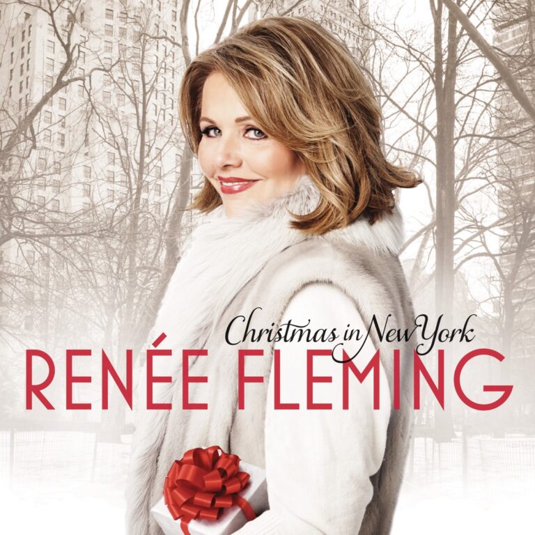 Renée Fleming in weißem Mantel mit Geschenk vor winterlicher Stadtkulisse.