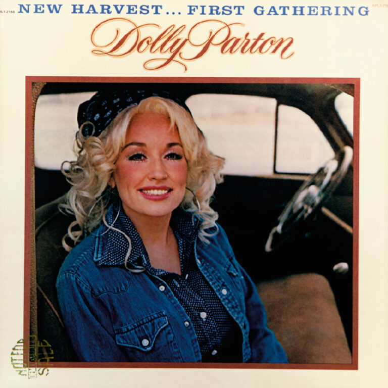 Dolly Parton lächelt in einem Auto, trägt eine Jeansjacke und hat lockige blonde Haare.