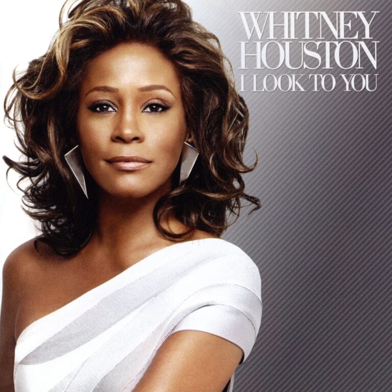 Porträt von Whitney Houston in einem weißen Kleid vor grauem Hintergrund.