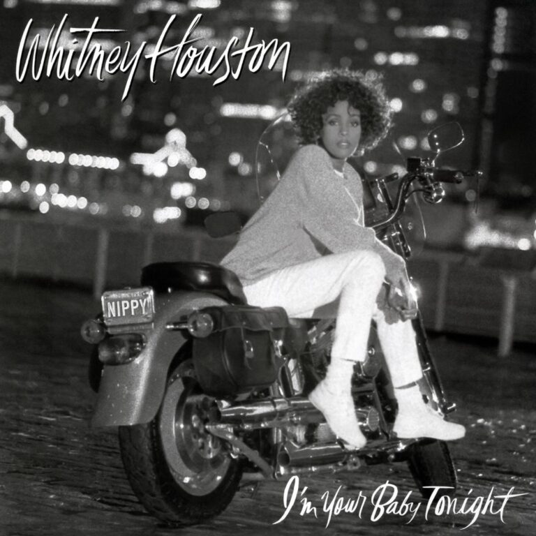 Whitney Houston sitzt auf einer Harley, trägt weiße Jeans und hat einen ausdruckslosen Gesichtsausdruck.