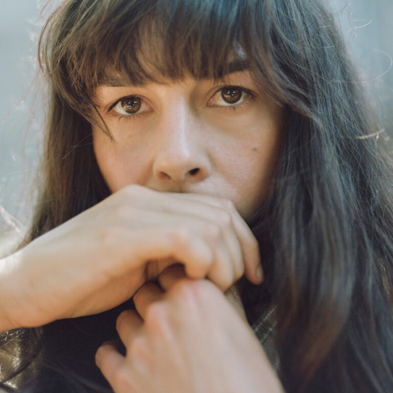 Nahaufnahme von Madi Diaz mit direktem, verletzlichem Blick in die Kamera. Ihre Hände sind vor dem Gesicht verschränkt – ein stilles Porträt zwischen Introspektion und roher Emotion.