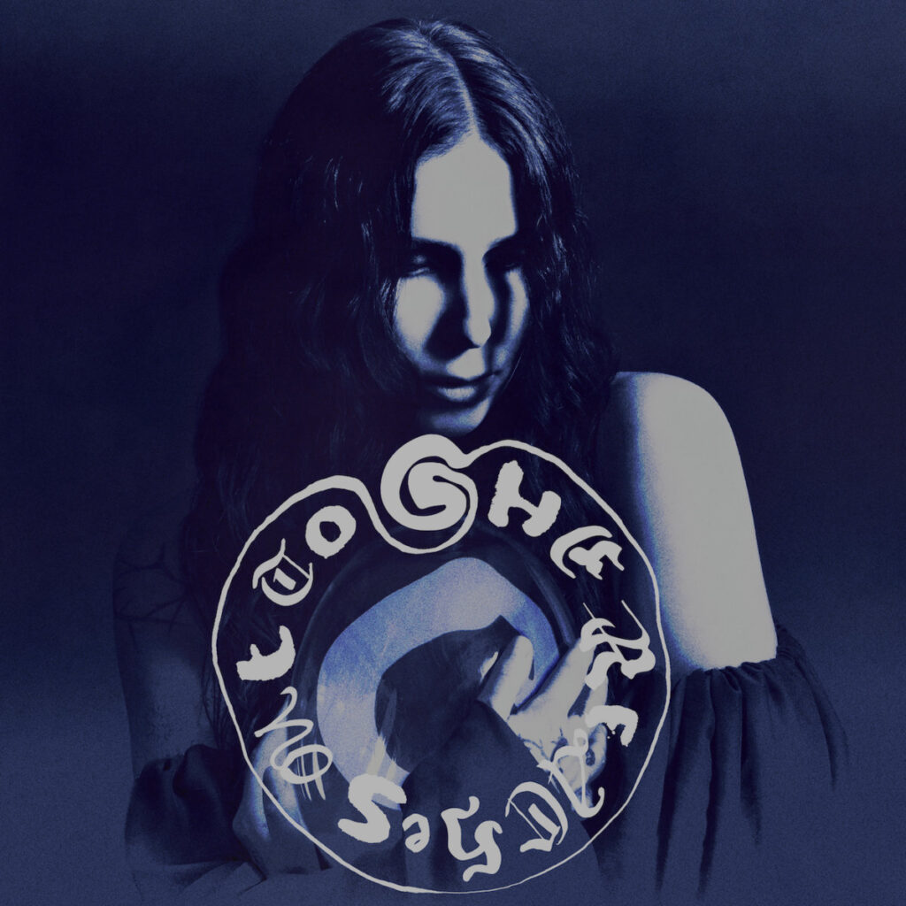 Cover von Chelsea Wolfe – She Reaches Out To She Reaches Out To She: geheimnisvolles Porträt in Blautönen mit verschlungenem Schriftkreis und düsterem Lichtspiel.