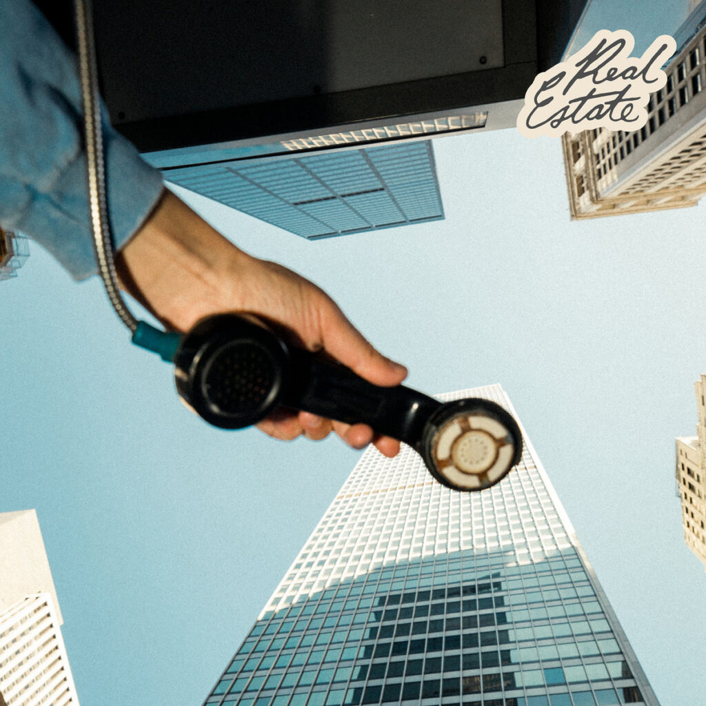 Albumcover von Real Estate – Daniel: Hand mit Telefonhörer ragt in den Himmel, umgeben von Hochhäusern, fotografiert aus der Froschperspektive.