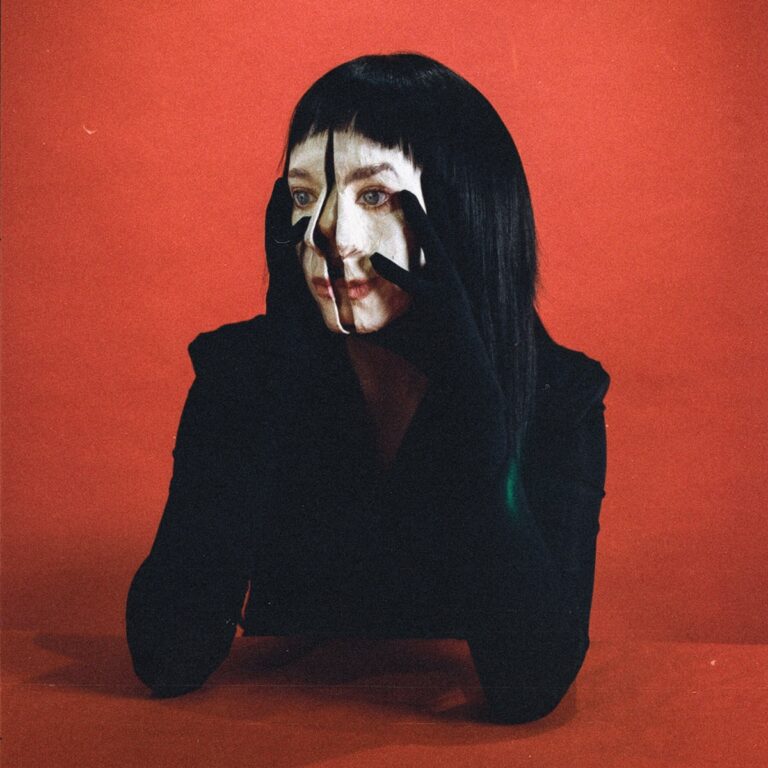 Porträt der Künstlerin Allie X vor rotem Hintergrund mit surreal verzerrtem Gesicht, inspiriert vom Cover ihres Albums „Girl With No Face“.