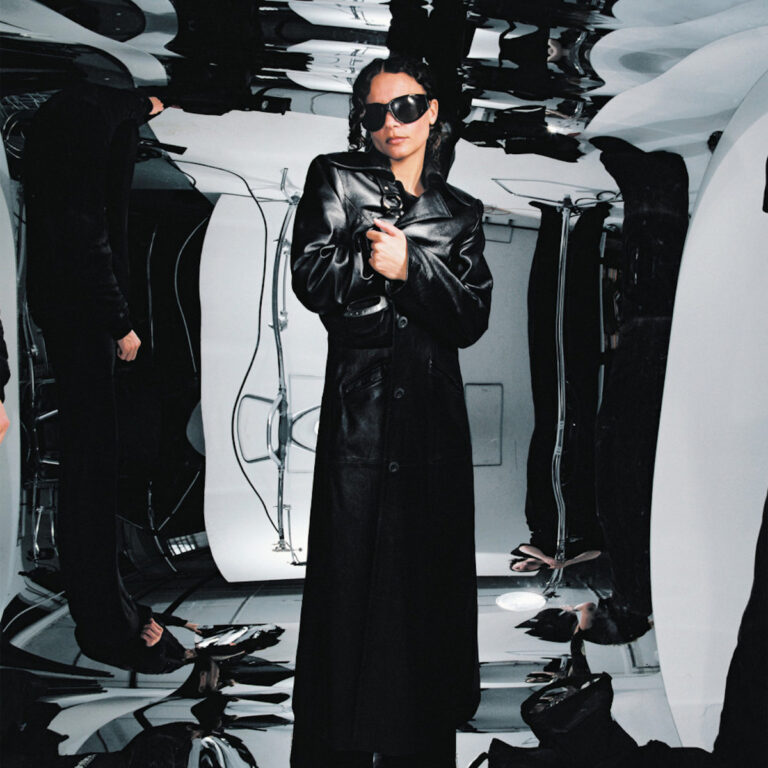Albumcover von Erika de Casier – Still: Die Künstlerin steht in schwarzem Ledermantel und Sonnenbrille in einem surreal verzerrten, monochromen Raum.