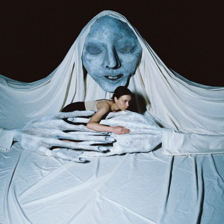 Albumcover von Abby Sage „The Rot“ mit surrealer Figur: die Künstlerin liegt in weißen Stoffarmen vor einem großen blauen Gesicht mit geschlossenen Augen.
