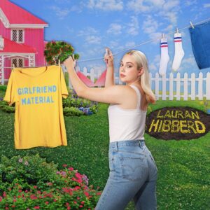 Albumcover von Lauran Hibberd – Girlfriend Material mit pinkem Haus, gelbem Shirt auf der Leine und der Künstlerin im Garten zwischen Retro-Kitsch und Ironie.