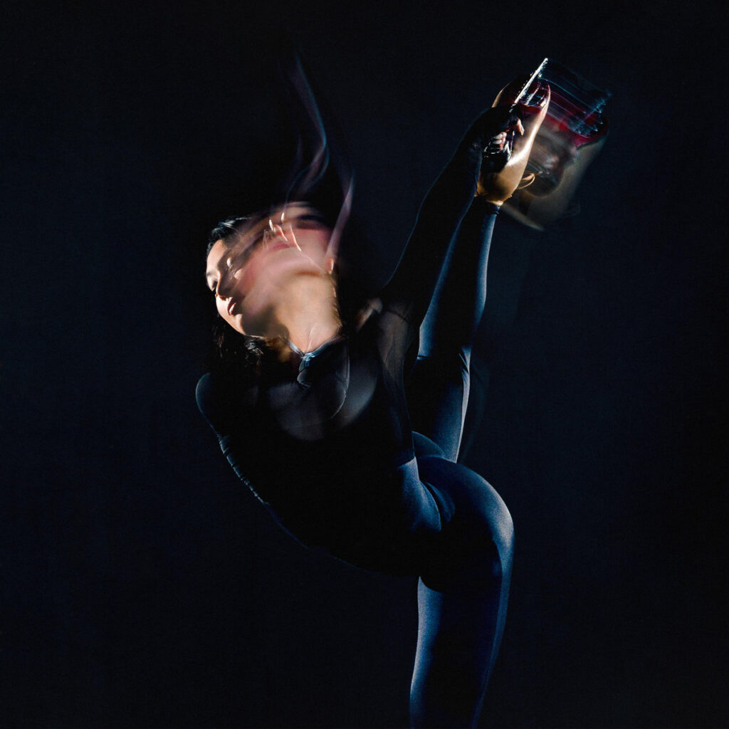 Albumcover von Kelly Moran – Moves in the Field zeigt eine verschwommene Figur in schwarzem Outfit, die in tänzerischer Pose ein Weinglas in die Luft hält, vor dunklem Hintergrund.