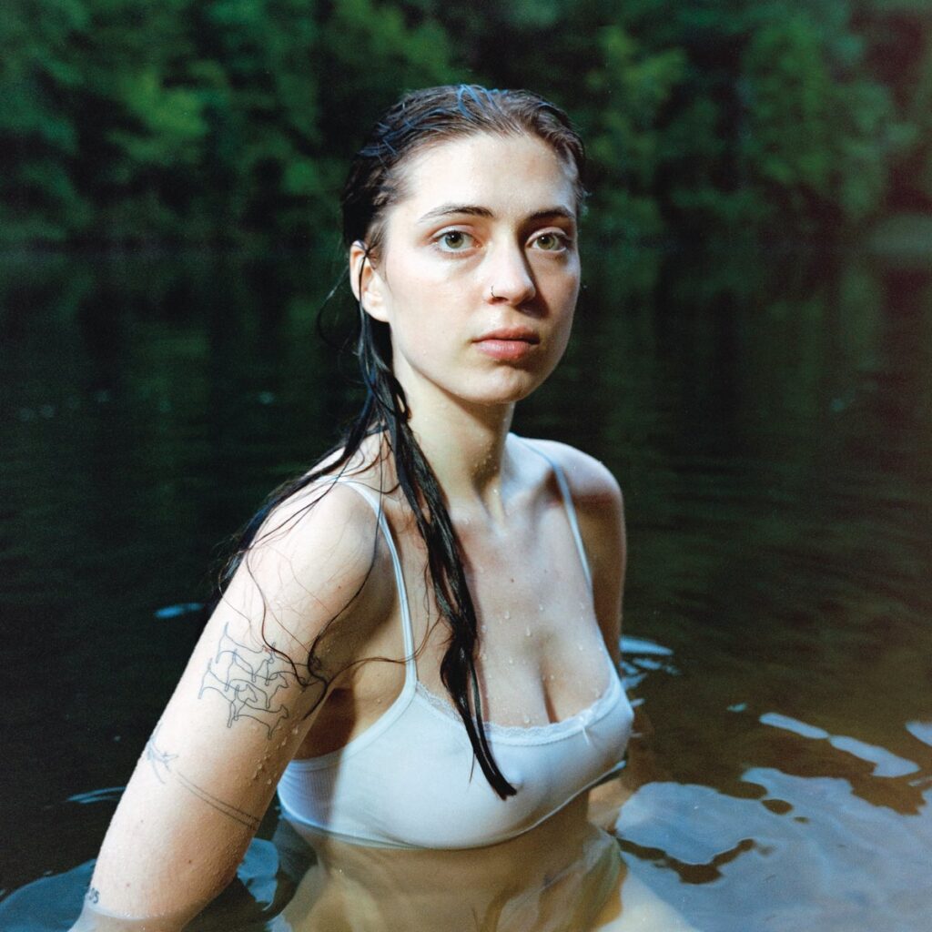 Lizzy McAlpine steht mit nassem Haar und weißem Top im Wasser, der Blick ruhig und direkt – ein ehrliches und ungeschöntes Cover zu Older.