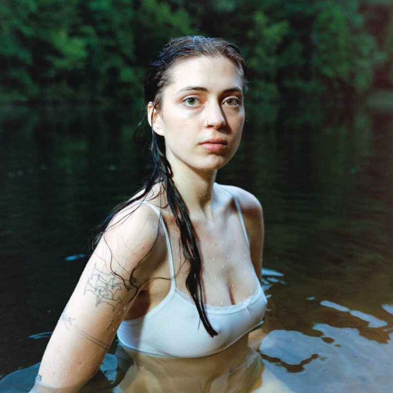 Lizzy McAlpine steht mit nassem Haar und weißem Top im Wasser, der Blick ruhig und direkt – ein ehrliches und ungeschöntes Cover zu Older.