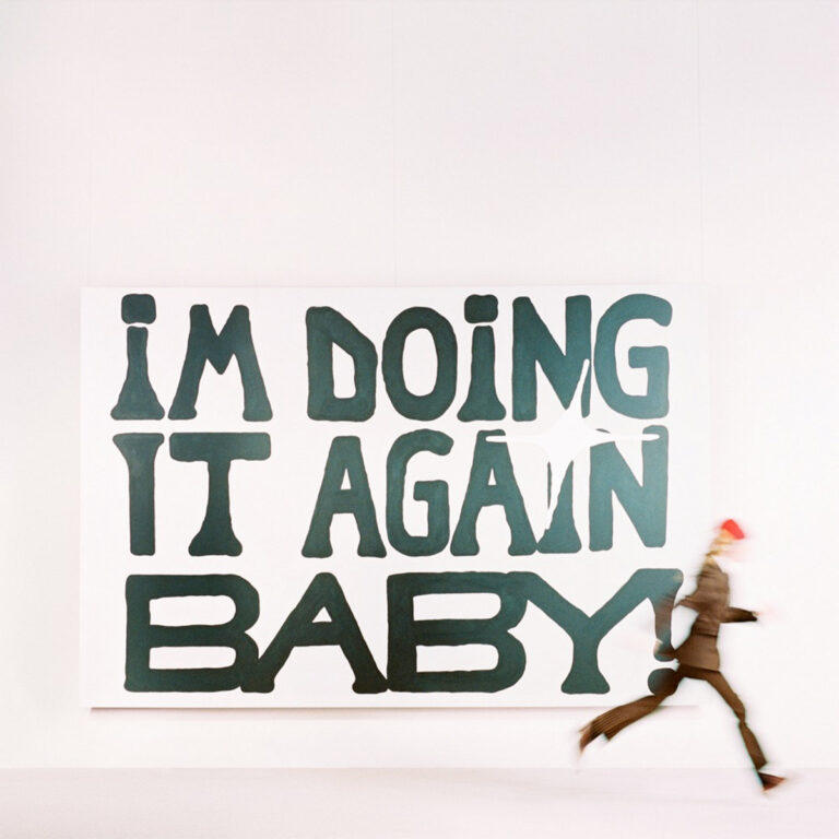 Albumcover von girl in red – I'm Doing It Again Baby! zeigt eine laufende Figur vor großem Wandbild mit dem gleichnamigen Schriftzug in verspielter Typografie.