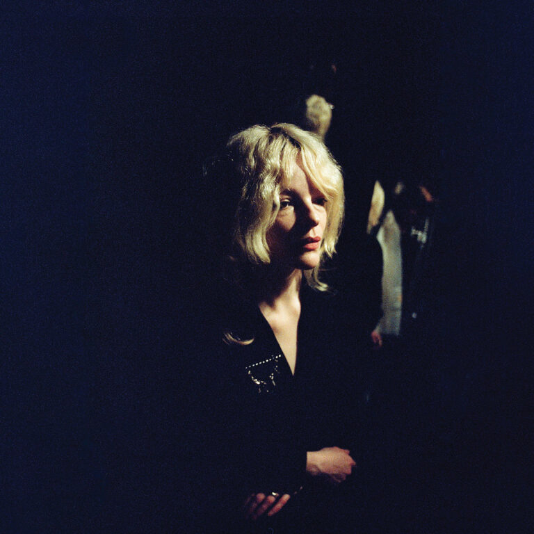 Jessica Pratt im Halbdunkel, mit verträumtem Blick und blonder Lockenmähne – ein mystisch-ruhiges Porträt auf dem Cover von „Here in the Pitch“.