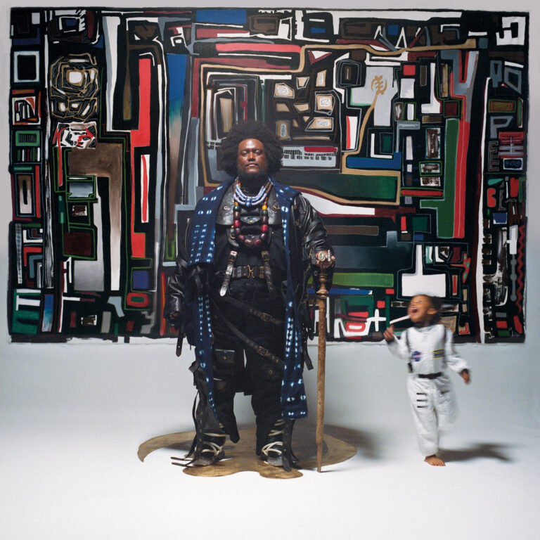 Cover des Albums „Fearless Movement“ von Kamasi Washington: Der Musiker steht in opulenter Kleidung vor einem farbenreichen abstrakten Wandgemälde, neben ihm ein lachendes Kind im Raumanzug.