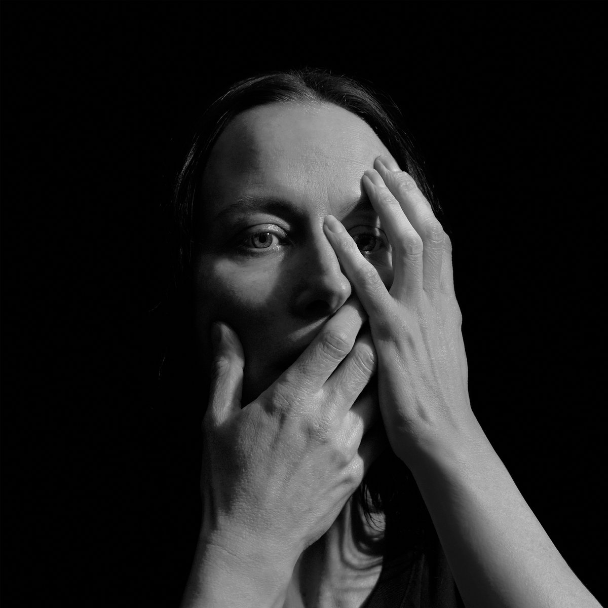Schwarz-weiß Portrait einer Frau mit beiden Händen vor Gesicht und Mund, symbolisiert emotionale Beklemmung und introspektive Tiefe.
