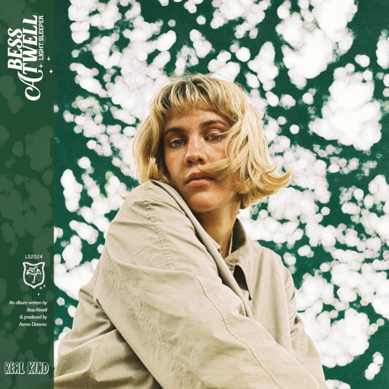 Cover von „Light Sleeper“: Bess Atwell im beigefarbenen Mantel vor grünem Himmel mit weißen, wolkenartigen Tupfern – ruhig, durchdacht, introspektiv.
