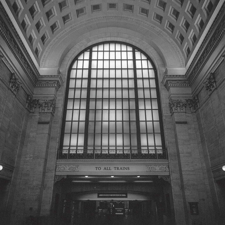 Cover des Albums „To All Trains“ von Shellac: Schwarzweiß-Foto einer monumentalen Bahnhofshalle mit großer Fensterfront und der Aufschrift „TO ALL TRAINS“.