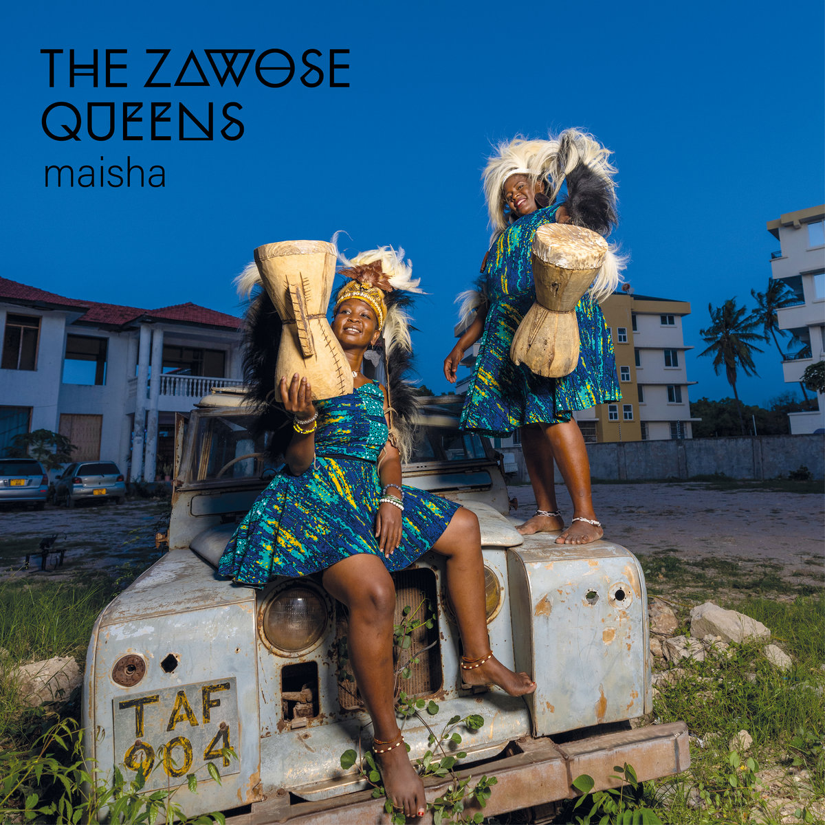 The Zawose Queens in traditioneller Kleidung mit Trommeln auf einem alten Jeep – das farbenfrohe Cover des Albums „Maisha“ strahlt Kraft und Freude aus.
