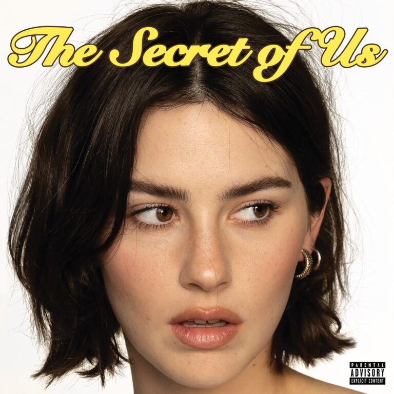 Gracie Abrams blickt seitlich mit leicht geöffnetem Mund, vor weißem Hintergrund – Albumcover The Secret of Us mit Retro-Schriftzug in Gelb über ihrem Kopf.