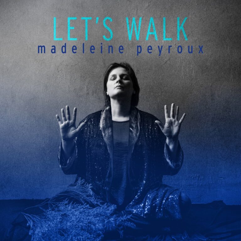 Madeleine Peyroux sitzt mit erhobenen Händen in meditativer Pose vor grauer Wand – das Cover des Albums „Let’s Walk“ in blauen Tönen gehalten.