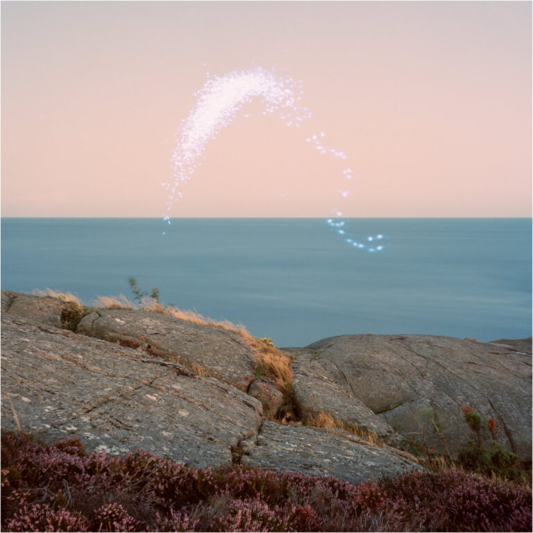 Blick auf eine felsige Küste bei Sonnenuntergang; über dem Meer schwebt eine helle, glitzernde Lichtform wie ein sanft leuchtendes Himmelszeichen.