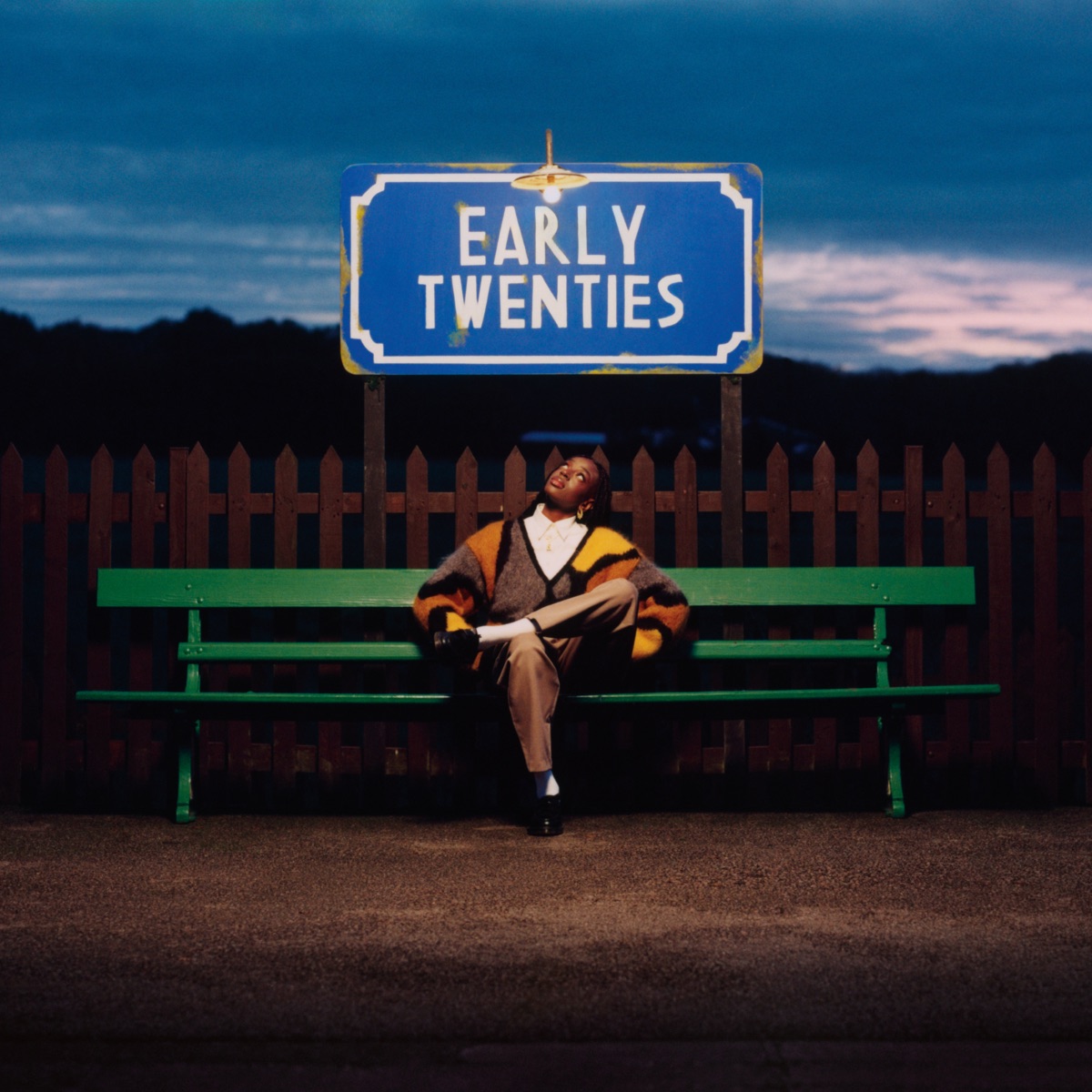 Das Cover von early twenties zeigt Cat Burns abends auf einer grünen Bank unter einem beleuchteten Schild mit dem Titel des Albums – eine Momentaufnahme zwischen Stillstand und Aufbruch.