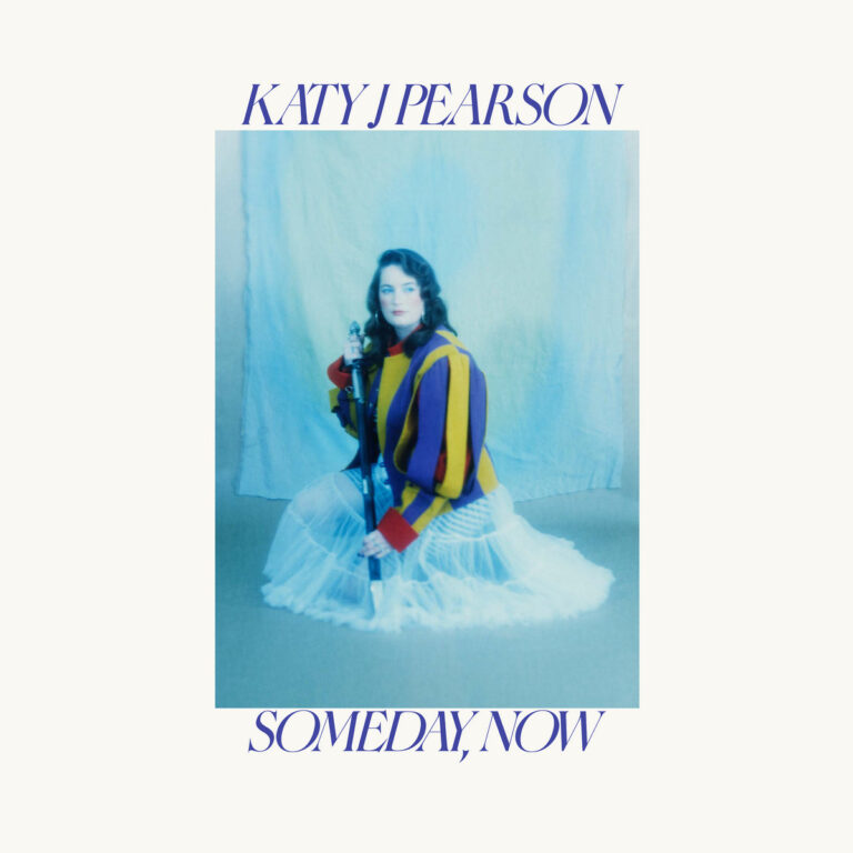 Katy J Pearson sitzt in weichem Licht auf dem Boden vor einem blauen Vorhang, trägt einen gestreiften Pullover und einen weißen Tüllrock – Cover von Someday, Now.