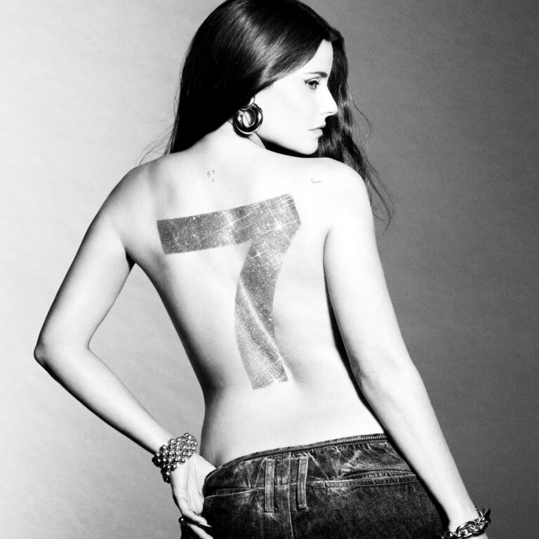 Cover von Nelly Furtados Album „7“: Die Sängerin in Jeans und mit freiem Rücken, auf dem eine glitzernde Sieben prangt – ikonisch, kontrastreich und selbstbewusst.