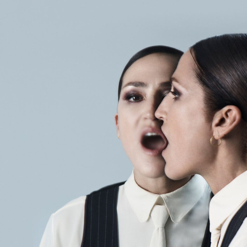 Joan As Police Woman vor grauem Hintergrund, ihr Gesicht gespiegelt mit offenem Mund – ein surreal-doppeltes Porträt auf dem Cover von Lemons, Limes and Orchids.