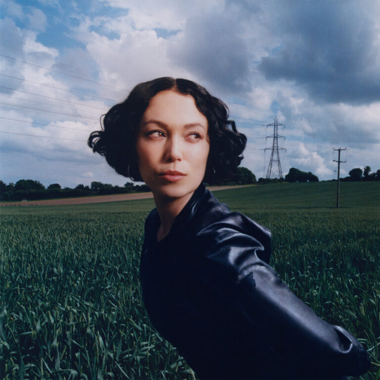Kelly Lee Owens blickt über ein weites Feld mit dramatischem Himmel – Coverfoto ihres Albums „Dreamstate“, das atmosphärische Elektronik und emotionale Tiefe vereint.