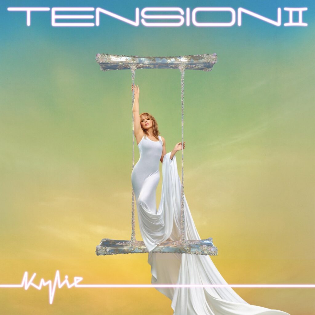 Kylie Minogue in weißem Kleid auf einer glitzernden Schaukel vor pastellfarbenem Himmel – Cover des Albums Tension II, ein Mix aus Eleganz und Pop-Fantasie.
