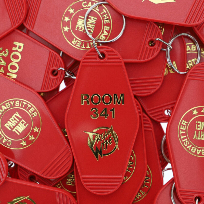 Rote Retro-Schlüsselanhänger mit goldener Prägung „ROOM 341“ und „CALL THE BABYSITTER – PARTY TIME!“ – Artwork zur Single „Room 341“ von Dream Wife.