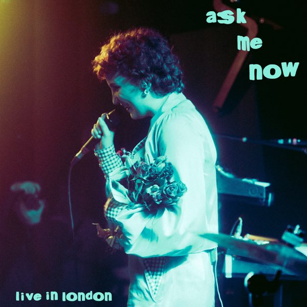 Cover der Live-EP „Ask Me Now“ von Phoebe Green, zeigt sie mit Mikrofon und Blumenstrauß auf einer Bühne in London, in weichem, buntem Bühnenlicht.