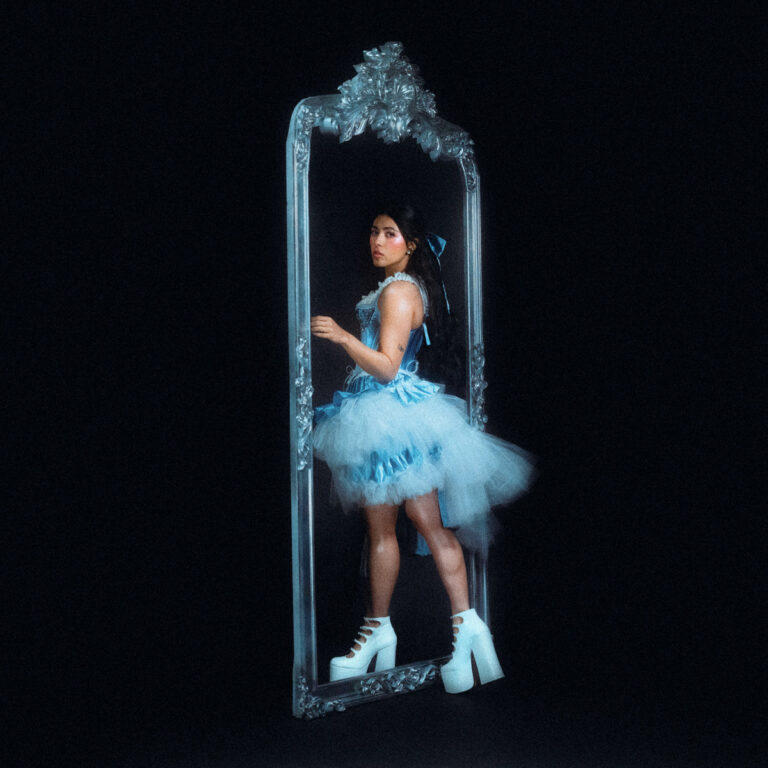 Mia Berrin von Pom Pom Squad im blauen Tutu vor einem verzierten Spiegel, symbolisch für Selbstreflexion – Artwork zum Album Mirror Starts Moving Without Me.